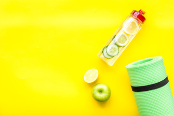 Healthy fruit water for sport, fitness. Bottle of water with lemon and cucumber near sport equipment on yellow background top view copy space