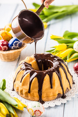 Delicious holiday slovak and czech cake babovka with chocolate glaze. Pouring chocolate topping. Easter decorations - spring tulips and eggs.