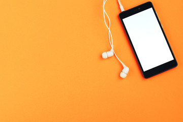 Smartphone and headphones on an orange background. Top view, space for text