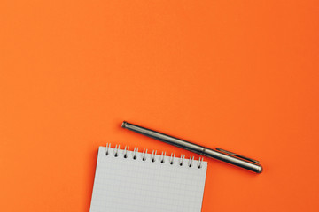 White sheet of notebook and pen on orange background.  Flat lay composition.