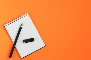 White sheet of notebook and pen on orange background.  Flat lay composition.