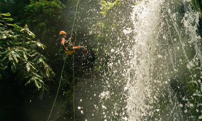  man canyoning. coming down the rope from the waterfall
