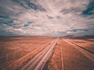 aerial drone shot of a highway traveling off into the distance with cars and vehicles into the blue skies with clouds and mountains