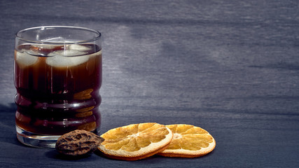 Drink with ice in a stanie on a dark background and oranges.