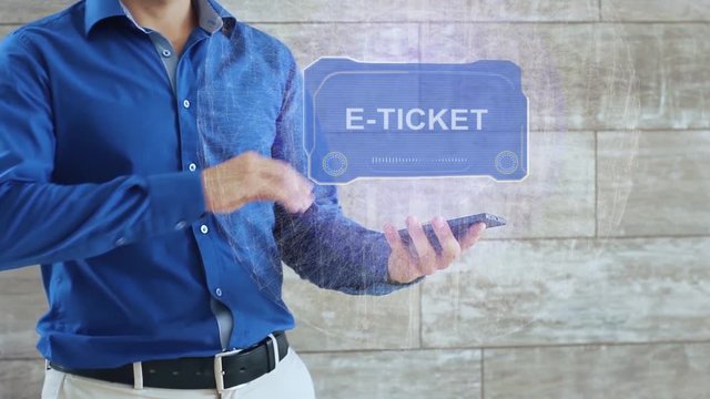 Man activates a conceptual HUD hologram with text E-ticket. The guy in the blue shirt and light trousers with a holographic screen on the background of the wall