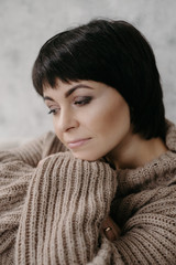 Gorgeous young brunette woman in warm knitted sweater posing on the bed in cozy appartments