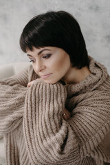 Gorgeous young brunette woman in warm knitted sweater posing on the bed in cozy appartments