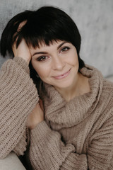 Gorgeous young brunette woman in warm knitted sweater posing on the bed in cozy appartments
