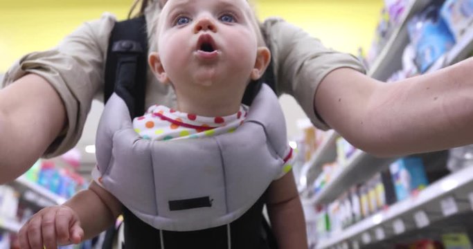 Mother And Baby Shopping In The Supermarket. Woman With A Daugther Makes The Choice When Looks Cart Around Store