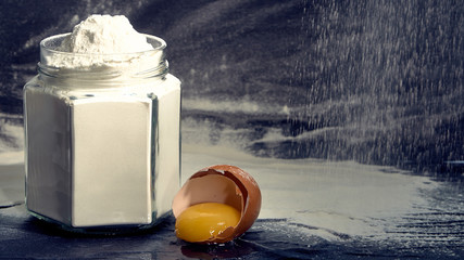 Flour in a jar with a broken egg on a dark background.