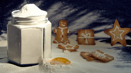 Flour in a jar with a broken egg and curly biscuits on a dark background.