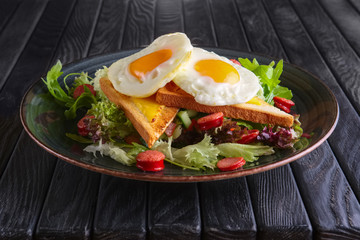 Fried eggs with toast, melted cheese and salad leaves