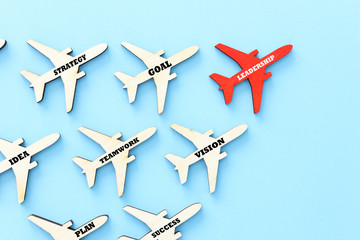 Leadership concept with airplanes on blue wooden background. One red leader flays ahead others.