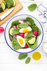 Fresh spring salad with spinach, radish, cucumber and egg. Delicious lunch, healthy food, summer vegetables. In bowl on white background