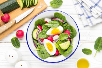 Fresh spring salad with spinach, radish, cucumber and egg. Delicious lunch, healthy food, summer vegetables. In bowl on white background