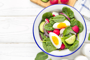 Fresh spring salad with spinach, radish, cucumber and egg. Delicious lunch, healthy food, summer vegetables. In bowl on white background