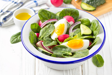 Fresh spring salad with spinach, radish, cucumber and egg. Delicious lunch, healthy food, summer vegetables. In bowl on white background