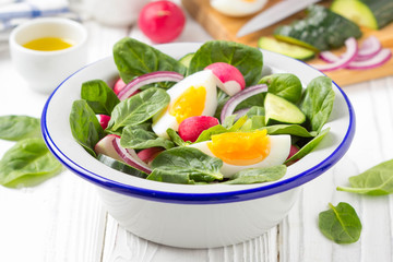 Fresh spring salad with spinach, radish, cucumber and egg. Delicious lunch, healthy food, summer vegetables. In bowl on white background
