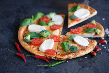 Sliced pizza with Mozzarella cheese, tomatoes, broccoli, Spices and fresh basil. Italian pizza. Pizza on black stone background
