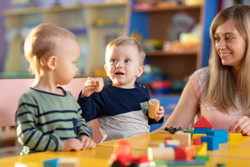 Fototapeta na wymiar Nursery babies kids playing with teacher in kindergarten