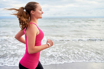 Fototapeta na wymiar Happy fitness woman runner running at seaside, copy space. Girl working out on beach at summer morning, side view. Healthy lifestyle concept