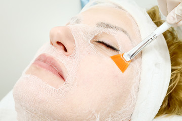beautician worker holding paintbrush  applying facial cosmetic serum  in biological treatment to female client in beauty salon