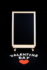 Chalkboard on stand, Heart shape and Wooden letters word "VALENTINE DAY" on black background