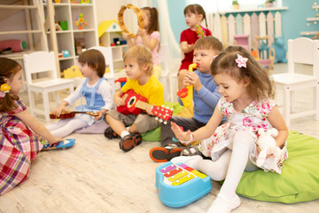 Children learning musical instruments on lesson in kindergarten or daycare - obrazy, fototapety, plakaty