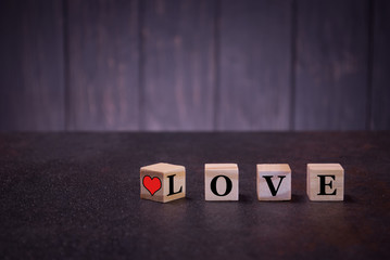 The word love and sigh red heart on wooden cubes, on a dark background, light wooden cubes signs,...
