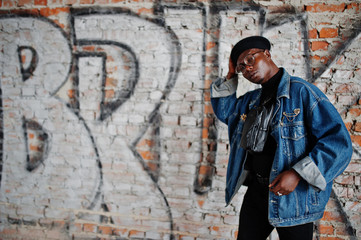 African american man in jeans jacket, beret and eyeglasses against graffiti brick wall with bruk sign. - obrazy, fototapety, plakaty