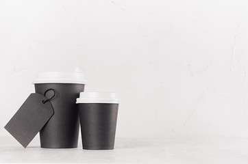 Coffee mockup - different size black paper cups with white cap and blank label on white wood table with copy space, coffee shop interior. 