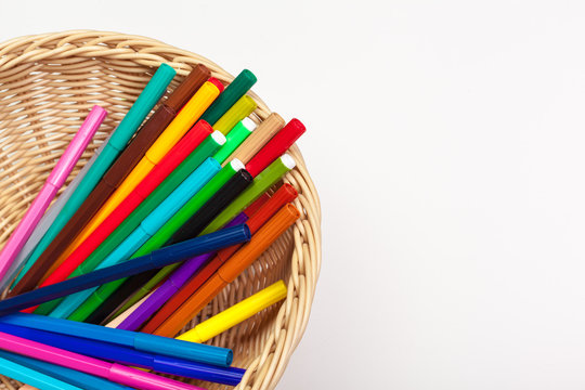 Lot of colorful markers in a wooden basket on white background