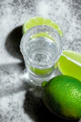 Tequila silver shots with lime slices and salt on wooden board