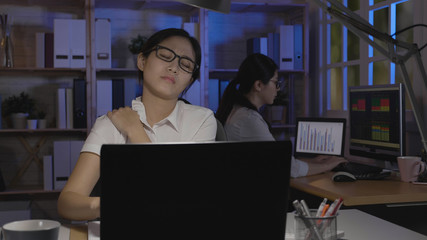 Fototapeta na wymiar tired exhausted stressed young female worker suffer from neck pain. businesswoman massaging painful shoulder sit at desk in dark office body health care concept. coworker typing on laptop computer