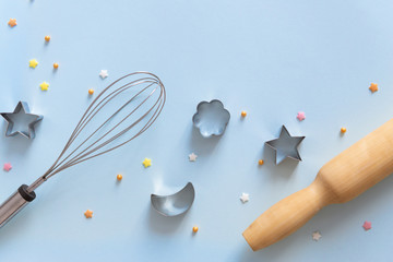 Metallic cookie cutters different shapes, whisk and rolling pin on blue background. Bakery and confectioner concept. Copy space