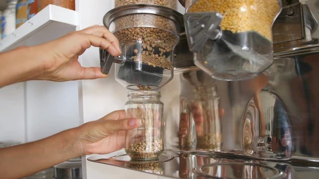 Female Pours Green Lentils from Vending Machine in a Glass Jar. Young Vegan Woman Shopping at Zero Waste Shop. No plastic Conscious Minimalism Lifestyle Concept. 4K.