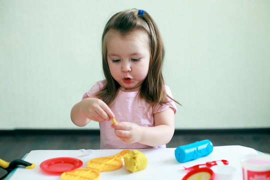 Cute affective emotional girl playing with play dought in her home. Concept of preschool education