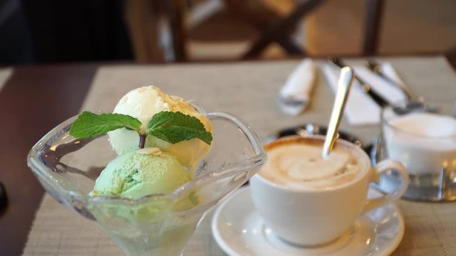Ice cream dessert in a cafe on the background of a cup of cappuccino coffee. Vanilla and pistachio ice cream balls with mint leaf