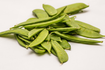 Close up of fresh organic green mange tout beans on a white background