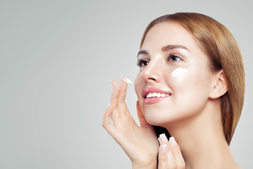 Obraz na płótnie Canvas Young beautiful woman with healthy clear skin applying moisturizing cream on her face. Female face closeup