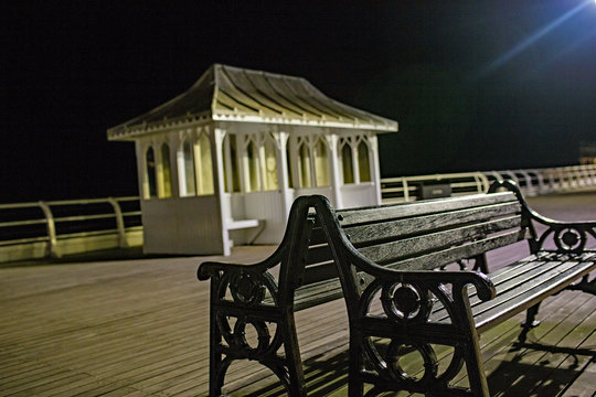 Close up of a wooden seat on the wooden  boards of a ier in front of the wooden shelter captured at night