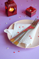 Empty pink plate, cutlery, hearts, candlesticks and red gift on pink-purple background. St. Valentine's Day table setting concept. Copy space