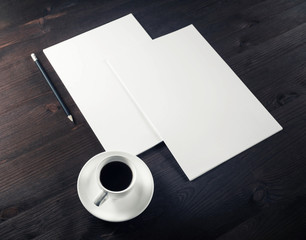 Blank letterheads, coffee cup and pencil on wooden background.