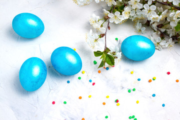 Purple blue Easter eggs, spring flowers apple, cherry, colorful candy on a white stone background