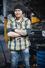 Fototapeta na wymiar Car repair service. Brutal mechanic man stands holding tools and smiles
