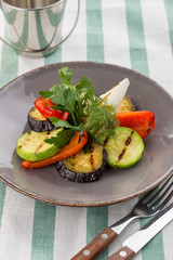 Grilled vegetables zucchini, bell pepper and fresh dill and parsley on the plate on textile background