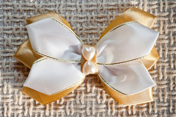 Hairpin for a bow of white and gold color on the background of coarse fabric, closeup shot