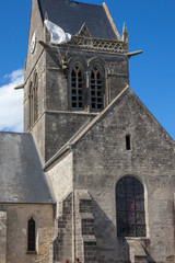 Fototapeta na wymiar Historic church of Sainte mere l'eglise, with a paratrooper hanging on the bell tower in Normady, France.