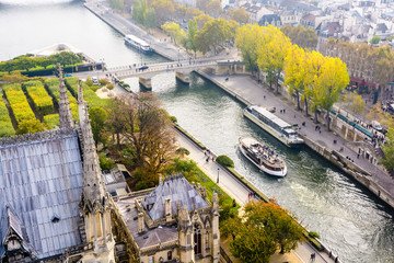 Aerial view from the tower of Notre-Dame de Paris cathedral over the river Seine with tour boats cruising and people strolling on the wharfs by a misty morning.