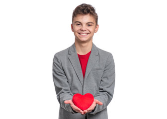 Happy Valentines Day. Cute young Teen Boy in Love with Red plush Heart in his hands. Smiling Child in grey suit, looking at camera, isolated on white background.